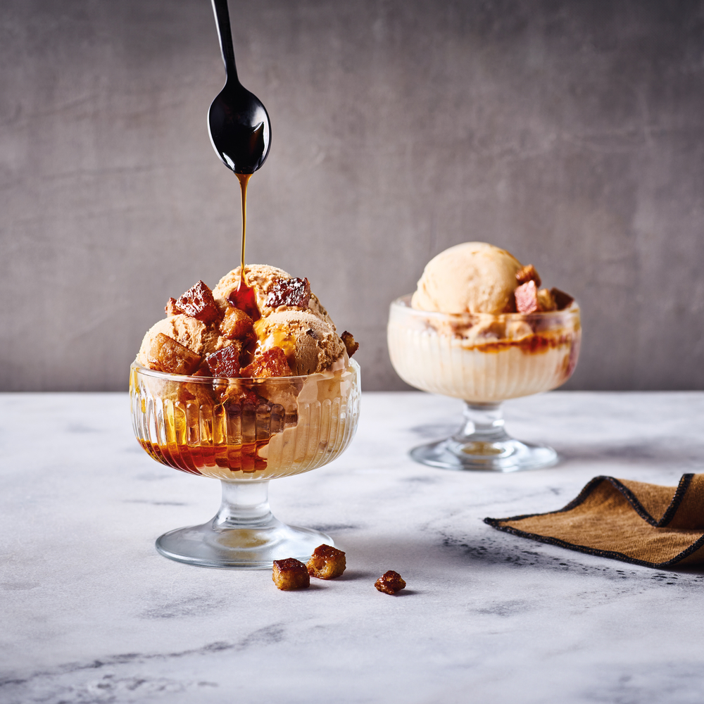 Two dessert glasses with ice cream and caramel sauce on a marble surface.